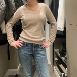 Beige v-ringad kashmirtröja från Repeat - Säljer en supermjuk och stilren beige v-ringad tröja från Repeat i kashmir. Tröjan har lång ärm och ribbade muddar vid ärmslut och nederkant. Perfekt för dig som gillar klassiska och bekväma plagg. Storlek 40 men passar mig som bär S