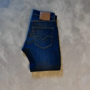 Levi's 512 blå jeans - Säljer ett par klassiska blå Levi's 512 jeans med raka ben och femficksmodell. Jeansen har en brun läderpatch bak i midjan och tydliga kontrastsömmar. Perfekta för dig som gillar tidlös denimstil. OBS!! W30 Uppsydda från L32 till L30.