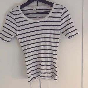 Vit och marinblå randig ribbad topp från Amisu - Säljer en vit ribbad topp från New Yorker med marinblå horisontella ränder. Toppen har rund halsringning och korta ärmar. Perfekt för en avslappnad och stilren look.