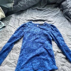 Blå spetsblus från Gina Tricot - Säljer en blå långärmad spetsblus från Gina Tricot. Blusen har ett vackert blommigt spetsmönster och rund halsringning. Perfekt för dig som vill ha en feminin och stilren topp i garderoben.