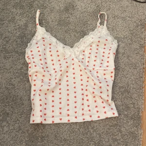 Linne  - Supersöt vit linnetopp med små röda hjärtan och spetsdetaljer längs v-ringningen. Tunt ribbat material och smala axelband. Perfekt för sommaren eller som nattlinne. Köpt på marknad vet ej vart den är ifrån 