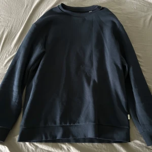 Svart sweatshirt från Jack & Jones - En stilren svart sweatshirt från Jack & Jones. Tröjan har rund halsringning, långa ärmar och ribbade muddar vid ärmslut och nederkant. Perfekt för en enkel och avslappnad look.