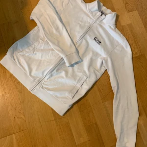 Vit ziptröja från EA7 Emporio Armani - Säljer en stilren vit ziptröja från EA7 Emporio Armani. Tröjan har dragkedja framtill, två fickor och en diskret logga på bröstet. Perfekt för en clean och sportig look.