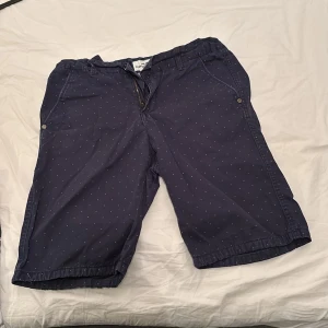 Mörkblå shorts med små prickar från Hampton Republic - Mörkblå shorts från Hampton Republic med diskret prickigt mönster. Modellen har resår i midjan, dragkedja och knäppning samt sidofickor och bakfickor. Perfekta för varma dagar.