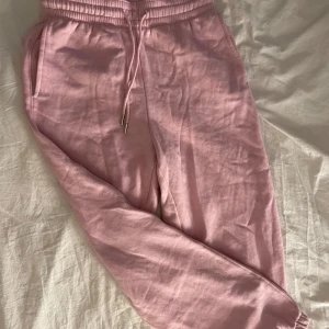 Rosa mjukisbyxor med dragsko - Säljer ett par ljusrosa mjukisbyxor med resår i midjan och benslut samt dragsko framtill. Byxorna har sidofickor och är tillverkade i mjuk bomull, perfekta för en avslappnad stil. De har ALDRIG använts, helt nya!