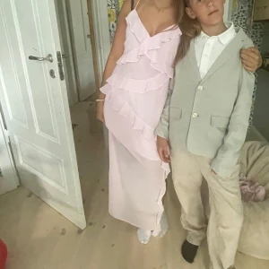 Ljusrosa långklänning med volanger - Säljer en ljusrosa långklänning med smala axelband och flera lager volanger framtill. Har bara använt en gång, har gått upp lite vid sidan men inget som syns, fråga gärna om fler bilder eller om ni har frågor. Köpte för 700kr men priset kan diskuteras 