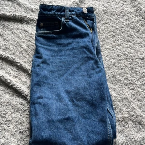 Blå raka jeans - Säljer ett par klassiska blå jeans med raka ben och normal passform. Byxorna har gylf med dragkedja och knapp, samt vanliga fickor fram och bak. Perfekta för en enkel och stilren look.