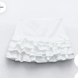 Vit volangkjol - Supersöt vit kjol med flera lager volanger som ger en lekfull och trendig look. Kjolen är kort och passar perfekt till varmare dagar eller när du vill sticka ut lite extra. Enkel att matcha med olika toppar.