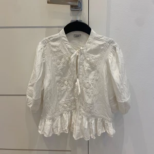 Vit knut blus med volanger - En fin och gullig blus med två knyten. Den har puffärmar och balanser längst ner och även lite broderier på framsidan. Köpt i Frankrike