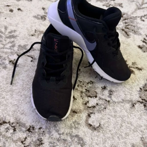 Svarta Nike sneakers med vit sula - Säljer ett par svarta Nike sneakers med vit och svart sula. Skorna har snörning och en diskret Nike-logga på sidan. Ovandelen är i syntetmaterial och mesh för bra andningsförmåga. Perfekta för vardagsbruk eller träning.