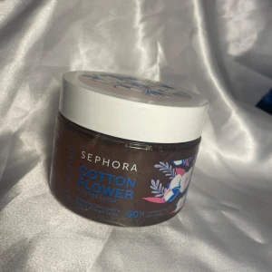 Sephora Cotton Flower body scrub - En burk med kroppsskrubb från Sephora i doften Cotton Flower. Burken är brun med vitt lock och har ett blommigt mönster i blått och rosa på etiketten. Innehåller 90% ingredienser av naturligt ursprung.