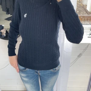 Mörkblå kabelstickad tröja från U.S. Polo Assn. - Säljer en mörkblå kabelstickad tröja från U.S. Polo Assn. i 100% bomull. Tröjan har lång ärm, rund hals och en liten broderad logga på bröstet. Perfekt för lager-på-lager och enkel att matcha med jeans. Aldrig använd 