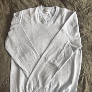 Ljusblå v-ringad tröja från John Henric - Säljer en stilren ljusblå v-ringad tröja från John Henric. Tröjan har förstärkta armbågslappar och är tillverkad i 100% bomull. Perfekt för lager-på-lager och passar till många olika outfits. Fin färg och knappt använd. Namnad på lappen i nacken.