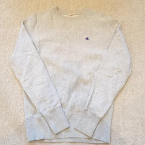 Grå sweatshirt från Champion - Säljer en klassisk grå sweatshirt från Champion med broderad logga på bröstet. Tröjan har rund halsringning och långa ärmar. Perfekt för en avslappnad och sportig stil.