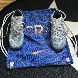 Nike Mercurial CR7 fotbollsskor - Säljer ett par Nike Mercurial CR7 fotbollsskor i grått och blått med orange detaljer. Skorna har snörning och mönstrad ovandel samt dobbar för spel på gräs. Perfekta för dig som vill sticka ut på planen! Elite!!