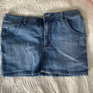 Blå jeanskjol med fickor - Säljer en klassisk blå jeanskjol med fem fickor och bälteshällor. Kjolen har en rak passform och stängs med dragkedja och knapp framtill. Perfekt att styla med en enkel topp eller hoodie.pris kan diskuteras 