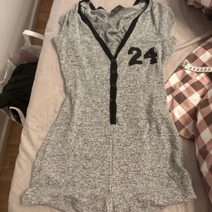 Grå body med tryck från max pink - Sportig gråmelerad body från Max Pink med svart v-ringning, knappar framtill och tryck med siffran 24 samt texten 'FLAWLESS' på ryggen. Perfekt för en avslappnad och cool stil.