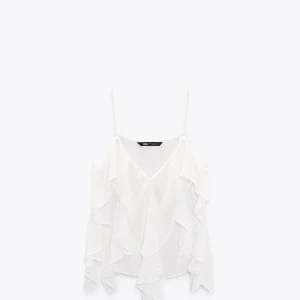 Vit volangblus från Zara - Säljer ett elegant vit volang linne från Zara med tunna axelband och v-ringning. Linnet har volangdetaljer och ett tunt somrigt material. Är i storlek S, har prislappen kvar och aldrig använts 