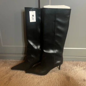 Svarta höga stövlar med klack - Säljer ett par svarta höga stövlar i skinnimitation med spetsig tå och smal klack, aldrig använda då jag råka beställa för stor strl! 