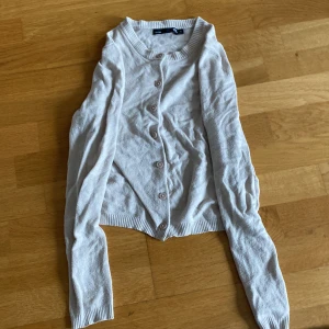 Beige kofta från 157 - Säljer en ljusbeige kofta från 157 i storlek XS. Koftan har långa ärmar, rund halsringning och knäppning framtill med matchande knappar. Perfekt att slänga över en topp när det blir lite kyligt.