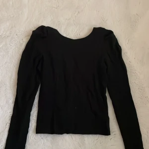 Svart långärmad topp från Lindex - Säljer en svart långärmad topp från Lindex med rundad halsringning och lätt rynkade detaljer vid axlarna. Toppen är i ett mjukt och stretchigt material, perfekt för en stilren look.