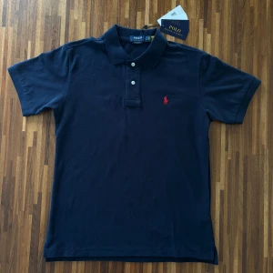 Mörkblå pikétröja från Polo Ralph Lauren - Klassisk mörkblå Ralph Lauren piké  |  Skick 10/10 (helt ny)  |  Size M  |  Custom slim fit  |  Bredd 48 cm  |  Längd 67 cm  | Perfekt för en stilren look till sommaren. Hör av dig vid minsta fråga eller fundering :)