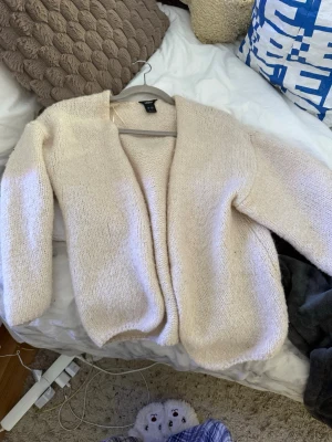 Beige stickad kofta från lindex ‼️RESERVERAD‼️ - Mysig beige stickad kofta från lindex med öppen front och avslappnad passform. Koftan har långa ärmar och är tillverkad i ett mjukt, fluffigt material som känns skönt mot huden. Perfekt att slänga på sig när det är lite kyligt ute.
