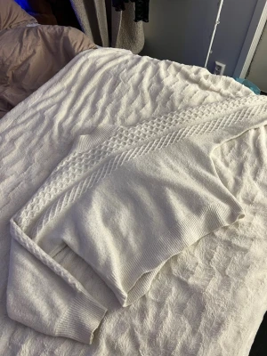 Vit stickad tröja från Kappahl - Säljer en vit stickad tröja från Kappahl med snyggt kabelstickat mönster över bröstet och ärmarna. Tröjan har ribbade muddar vid ärmslut och nederkant, perfekt för att hålla värmen. Enkel och stilren design som passar till mycket. Passar som M 