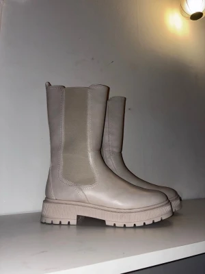 Beige chunky boots med resår Catwalk - Snygga beige boots med chunky sula och resår på sidorna. Stövlarna har dragkedja på insidan och är tillverkade i ett slätt, matt material som liknar skinn. Perfekta för dig som gillar stilrena och trendiga skor med lite högre skaft.