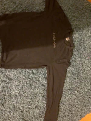 Svart långärmad tröja Calvin Klein - Snygg svart långärmad tröja från Calvin Klein med diskret logotyp på bröstet. Tröjan har rund halsringning och är tillverkad i mjukt material som känns skönt mot huden. Perfekt för en clean och stilren look.