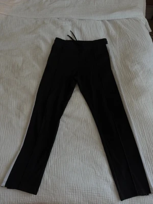 Svarta mjukisbyxor med dragkedja - Säljer ett par svarta mjukisbyxor med raka ben och dragkedjor vid bensluten. Byxorna har resår i midjan och snörning för bästa passform. 