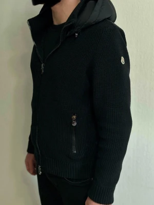 Moncler cardigan  - Moncler Cardigan – Sällsynt & Eftertraktad Modell – Strl M – Mycket Fint Skick  Säljer en exklusiv Moncler cardigan i mycket fint skick. Detta är en sällsynt och eftertraktad modell som kombinerar Monclers ikoniska design med hög komfort och premiumkvalitet.  Modellen har en stickad cardigan-konstruktion med dunfodrad fram- och bakpanel samt huva, vilket ger både värme och en elegant silhuett. Kombinationen av stickade ärmar och dunpaneler gör den perfekt som en stilren jacka för höst, vår eller