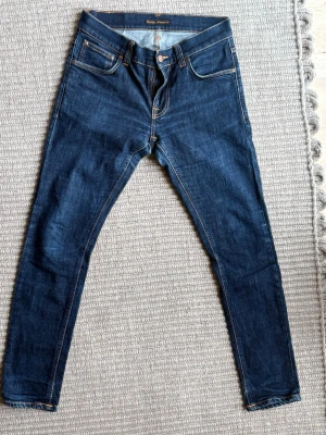 Mörkblå jeans Nudie 30,30 - Snygga mörkblå skinny jeans från Nudie Jeans med klassisk femficksmodell och kontrastsömmar. Jeansen har normal midja och är tillverkade i stretchigt denim för en bekväm passform. Perfekta till en avslappnad streetstyle-look.