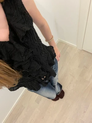 Svart volang topp - Säljer en svart ärmlös topp med volangdetaljer och strukturerat tyg. Toppen har en v-ringad hals Perfekt att styla med jeans eller kjol för en trendig outfit. Storlek 152 men passar som xxs /xs 