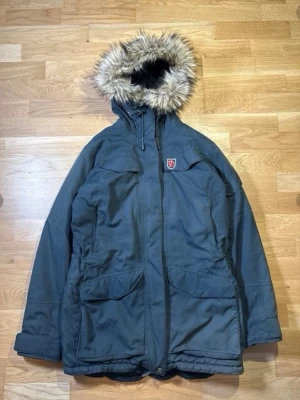 Fjällräven Nuuk Parka - Fjällräven Nuuk Parka i storlek S. En premium vinterjacka designad för mycket kallt väder, som kombinerar värme, hållbarhet och tidlös skandinavisk stil.  Perfekt för vinter, vardagsbruk, resor eller utomhusaktiviteter. Funktionell design med en ren, klassisk look som aldrig går ur modet. En pålitlig och högkvalitativ investeringsjacka.  Om du har några frågor om bilder eller mått, tveka inte att kontakta mig.  Skick som du kan se på bilderna  