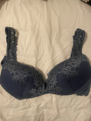Mörkblå spets-bh med vaddering Superpushup-behå Gioia Pretty Flowers - Snygg mörkblå bh med vadderade kupor och vackra spetsdetaljer både på kuporna och axelbanden. Bh:n har breda axelband för extra komfort och en klassisk knäppning bak. Perfekt för dig som gillar en feminin och stilren look.