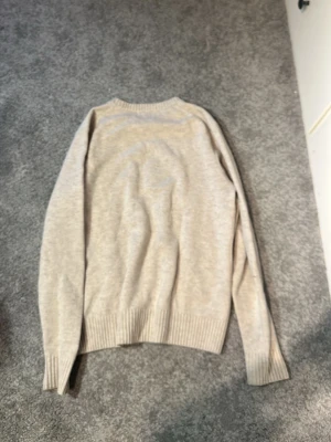 Beige stickad tröja - Snygg beige stickad tröja från Bläck i storlek M. Tröjan har rund halsringning och ribbstickade muddar vid ärmslut och nederkant. Perfekt för lager-på-lager och enkel att matcha med andra plagg.