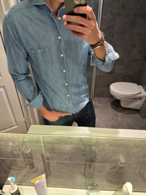 Ljusblå jeansskjorta med knappar - Säljer en stilren ljusblå jeansskjorta med klassisk krage och bröstficka från Eton. Riktigt snygg till sommar och vår. Jag på bilden är 188cm och bär storlek S. Hör av er vid fler frågor eller prisförslag:)