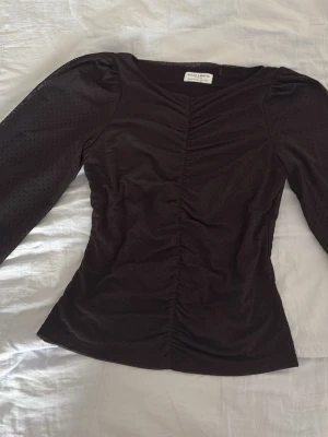 Svart långärmad blus från Holly & White - Snygg svart topp från Holly & White med lång lite genomskinlig ärm och diskret prickigt mönster i tyget. Toppen har rynkade detaljer framtill. Blusen är använd men i väldigt bra skick