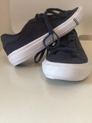 Marinblå sneakers från Björn Borg - Snygga marinblå sneakers från Björn Borg med klassisk låg profil. Skorna har vit sula, mörkblå snören och ovandel i textil. Perfekta för en clean och stilren look. Tidlös design som passar till det mesta.