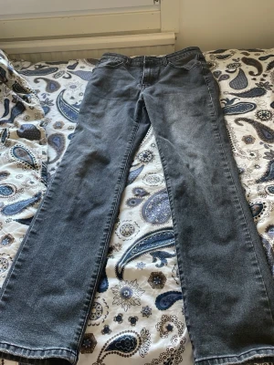 Grå raka jeans med fem fickor - Säljer ett par grå jeans med rak passform och klassisk femficksdesign. Jeansen har normal midja och subtila slitningar för en avslappnad look. Tillverkade i denim med en mjuk känsla. Perfekta för dig som gillar en enkel och stilren stil.