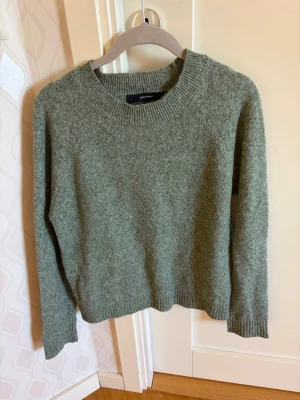 Grön stickad tröja från Vero Moda - Mysig grön stickad tröja från Vero Moda med rund halsringning och ribbstickade muddar vid ärmslut och nederkant. Perfekt för lager-på-lager och enkel att matcha med jeans eller kjol. Tröjan har en klassisk, rak passform och är tillverkad i mjukt material. Ställ gärna frågor💕