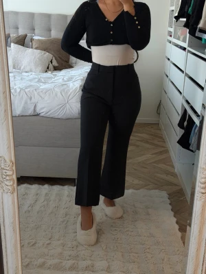 Svarta vida kostymbyxor - Snygga svarta kostymbyxor med hög midja och vida ben. Byxorna har en klassisk look med pressveck och stängs med dragkedja och knapp framtill. Perfekta för en stilren och trendig outfit.