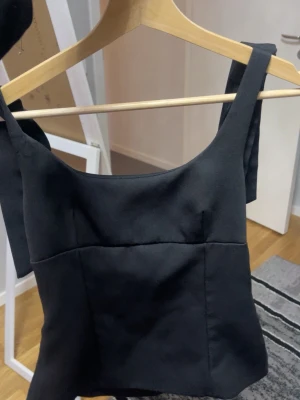 Svart top.  - Svart top med breda axelband som knyts på axlarna. 