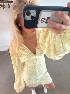 Gul adooreklänning  - Söt gul kortklänning med puffiga långärmar. Klänningen har knappar framtill och är figurnära i modellen. Perfekt för sommarens alla tillfällen. Storlek 36. Använd enstaka gånger