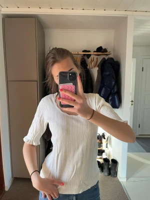 Vit ribbad topp med rund hals - Säljer en vit ribbad topp med rund hals och trekvarts ärmar. Perfekt att matcha med jeans eller kjol i sommar.