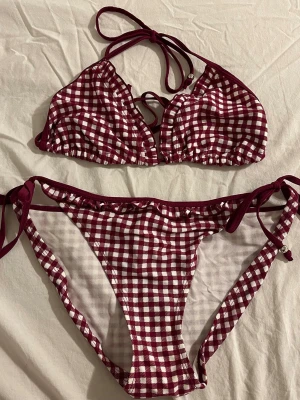NY! Rutig bikini - Closeness/Åhlens - Ny med lapp + plomberad! Supersnygg bikini med vinrött och vitt rutigt mönster. Klassisk trekantsmodell med knyt i nacken och ryggen, samt matchande bikinitrosa med knyt i sidorna. 