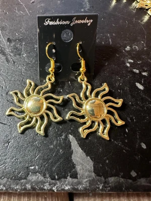 Solformade örhängen i guldton - Säljer ett par statement örhängen i metall med solformad design i glänsande guldton. Örhängena har krokfäste och är perfekta för dig som vill sticka ut med en unik accessoar. Passar till alla tillfällen där du vill addera lite extra shine till din look.