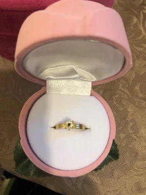 Guldfärgad ring med pärldetaljer - Snygg guldfärgad ring med en liten blomformad detalj i mitten, dekorerad med små pärlor. Ringen har en klassisk och elegant design som passar perfekt till din smyckessamling. Levereras i en söt rosa ask. Den är justerbar.