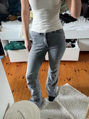 Grå bootcut jeans med hög midja - Säljer ett par grå bootcut jeans med hög midja och klassisk femficksdesign. Jeansen har en snygg tvättad look och raka ben som blir vidare nedtill. Perfekta för en avslappnad och trendig stil.